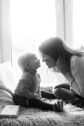 Smiling mother and toddler face-to-face, almost touching noses.