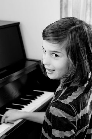 A young girl seated at the piano turns toward the camera, smiling.