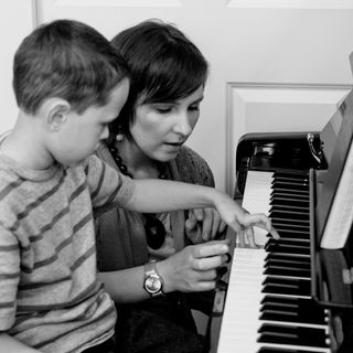 Susi Forshey points out a piano key while a young student watches closely.
